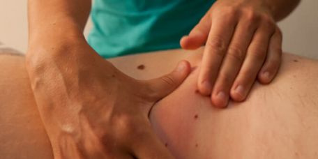 Therapeutin massiert Rücken eines Patienten in der manuellen Therapie