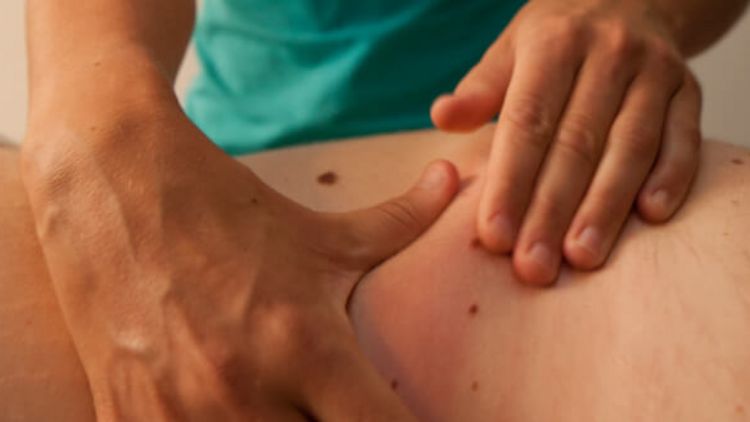 Therapeutin massiert Rücken eines Patienten in der manuellen Therapie