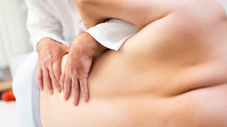 Arzt massiert Rücken eines Patienten bei der manuellen Therapie