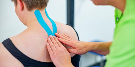Therapeut legt Kinesotape am Hals der Patientin an