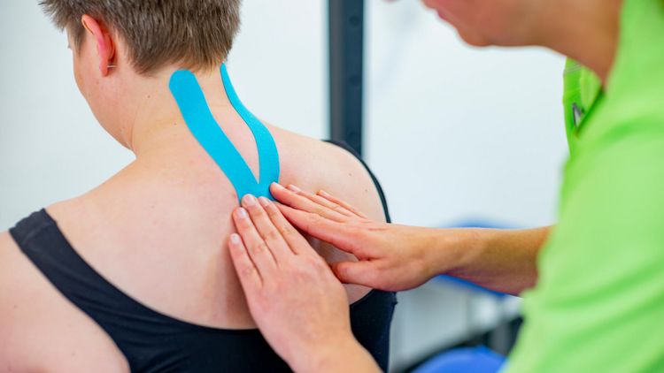 Therapeut legt Kinesotape am Hals der Patientin an